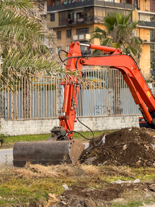 Urban Excavator Scooping Dirt Beside Palm Tree and Fence. High quality photo
